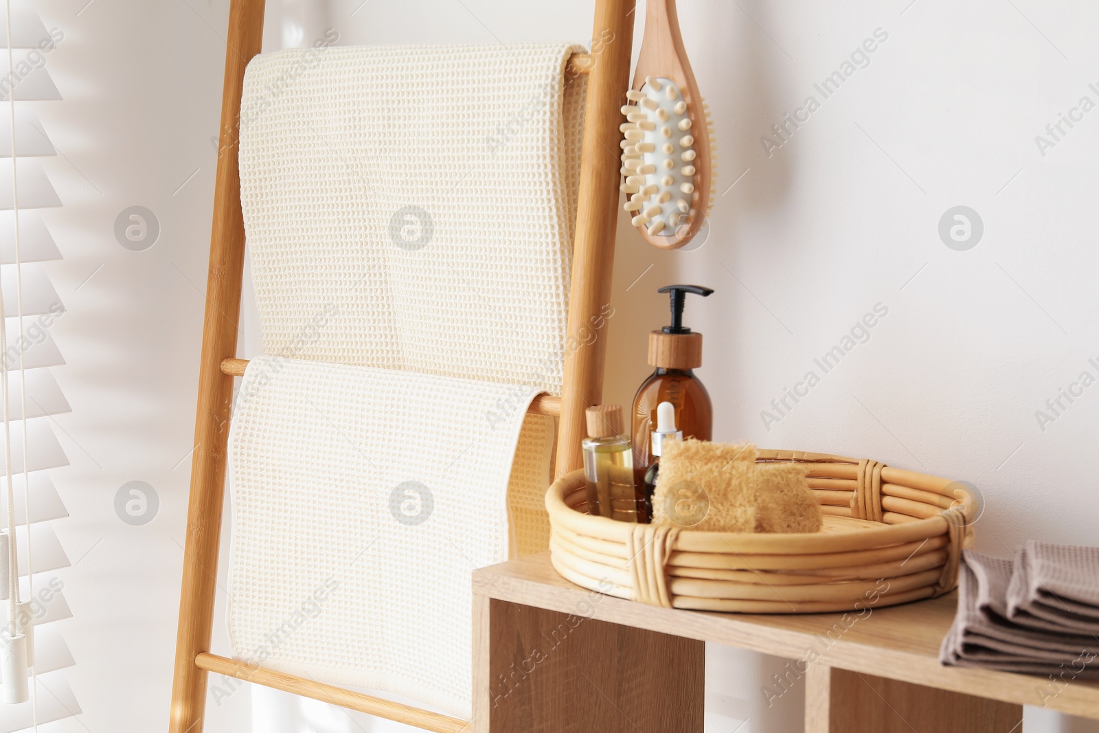 Photo of Clean waffle towels and spa products on shelving unit near white wall in bathroom