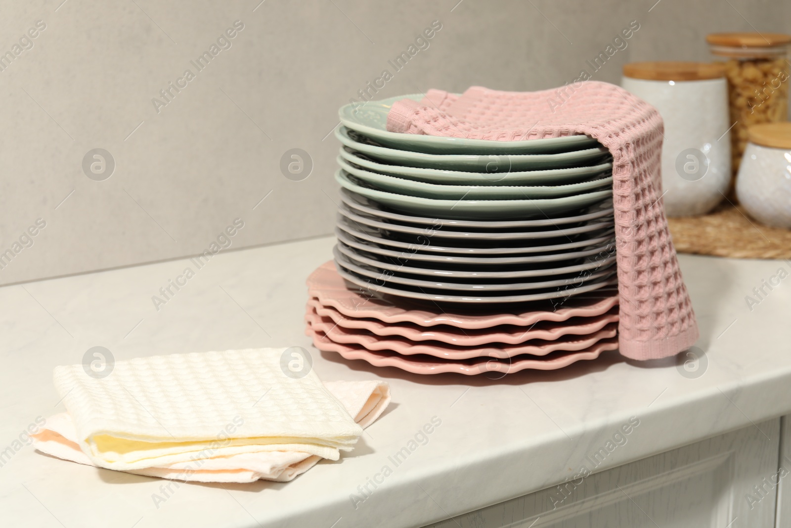 Photo of Waffle towels and stack of clean plates on white table near grey wall, closeup