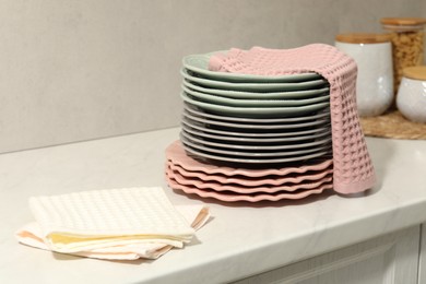Photo of Waffle towels and stack of clean plates on white table near grey wall, closeup
