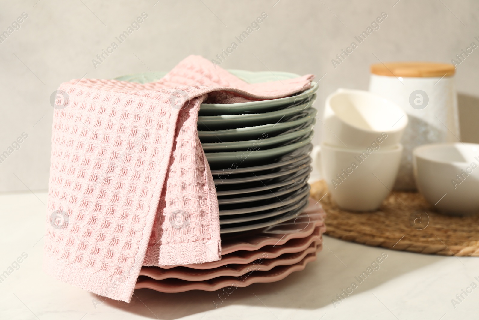 Photo of Pink waffle towel and stack of clean plates on white table near grey wall, closeup