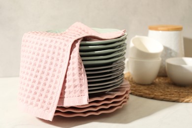 Photo of Pink waffle towel and stack of clean plates on white table near grey wall, closeup