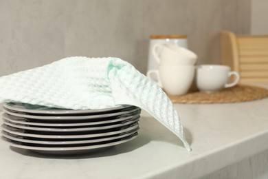Photo of Waffle towel and stack of clean plates on white table near grey wall, closeup