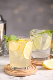 Photo of Tasty citrus cocktails in glasses on white marble table against blurred lights, closeup