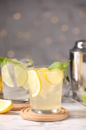 Photo of Tasty citrus cocktails in glasses on white marble table against blurred lights