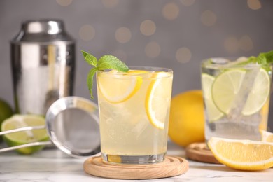 Photo of Tasty citrus cocktails in glasses on white marble table against blurred lights, closeup