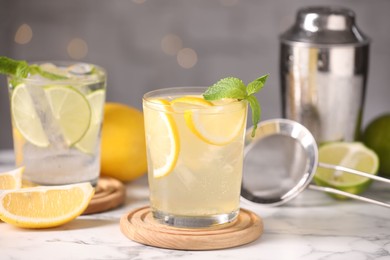 Photo of Tasty citrus cocktails in glasses on white marble table against blurred lights, closeup