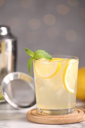 Photo of Tasty cocktail with lemon slices and mint in glass on white marble table, closeup
