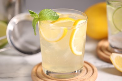 Photo of Tasty cocktail with lemon slices and mint in glass on white table, closeup