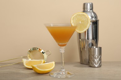 Photo of Tasty lemon cocktail in glass and bartender equipment on wooden table against beige background, closeup