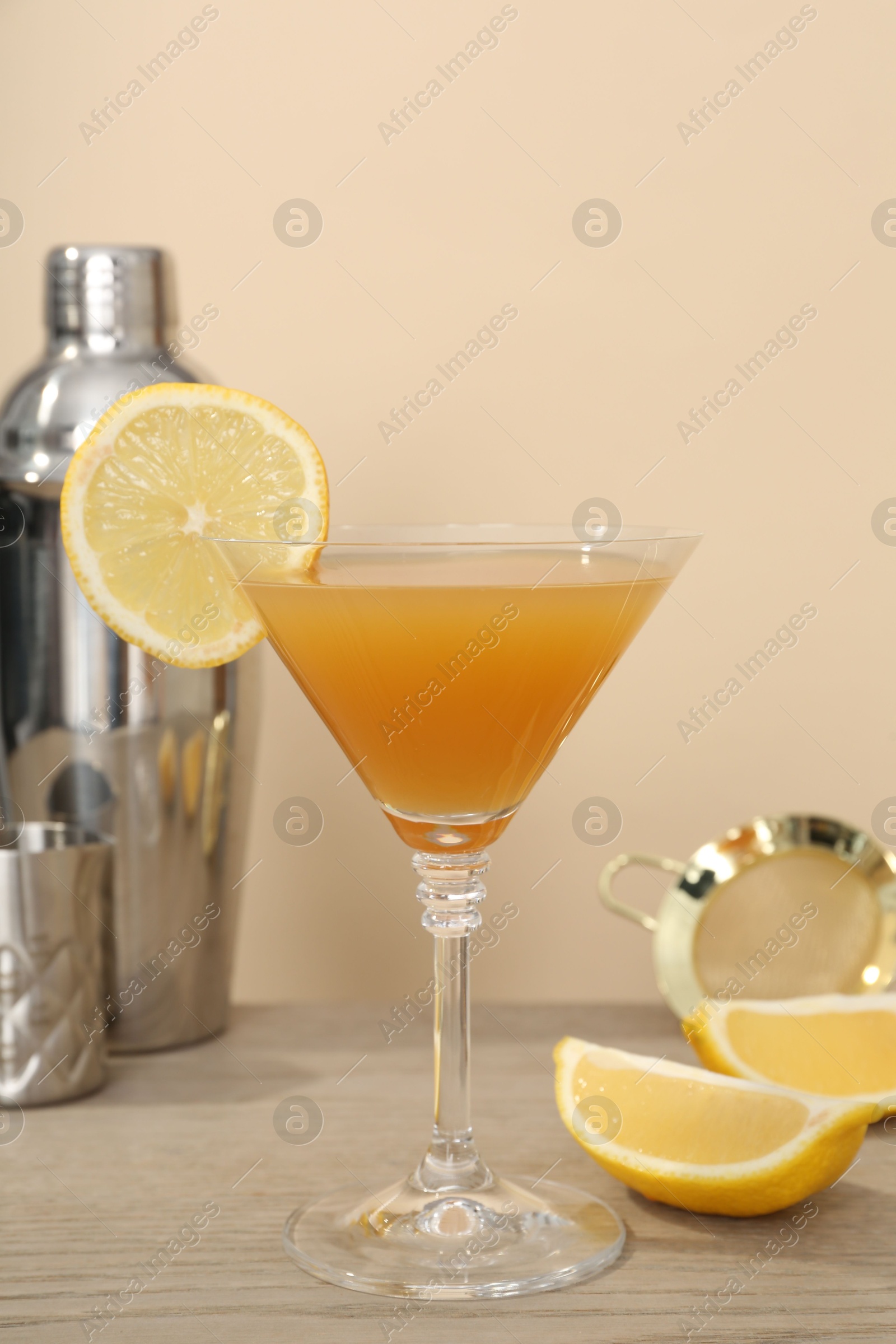 Tasty lemon cocktail in glass and bartender equipment on wooden table against beige background, closeup Photo of Tasty lemon cocktail in glass and bartender equipment on wooden table against beige background, closeup