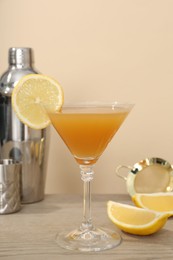Photo of Tasty lemon cocktail in glass and bartender equipment on wooden table against beige background, closeup