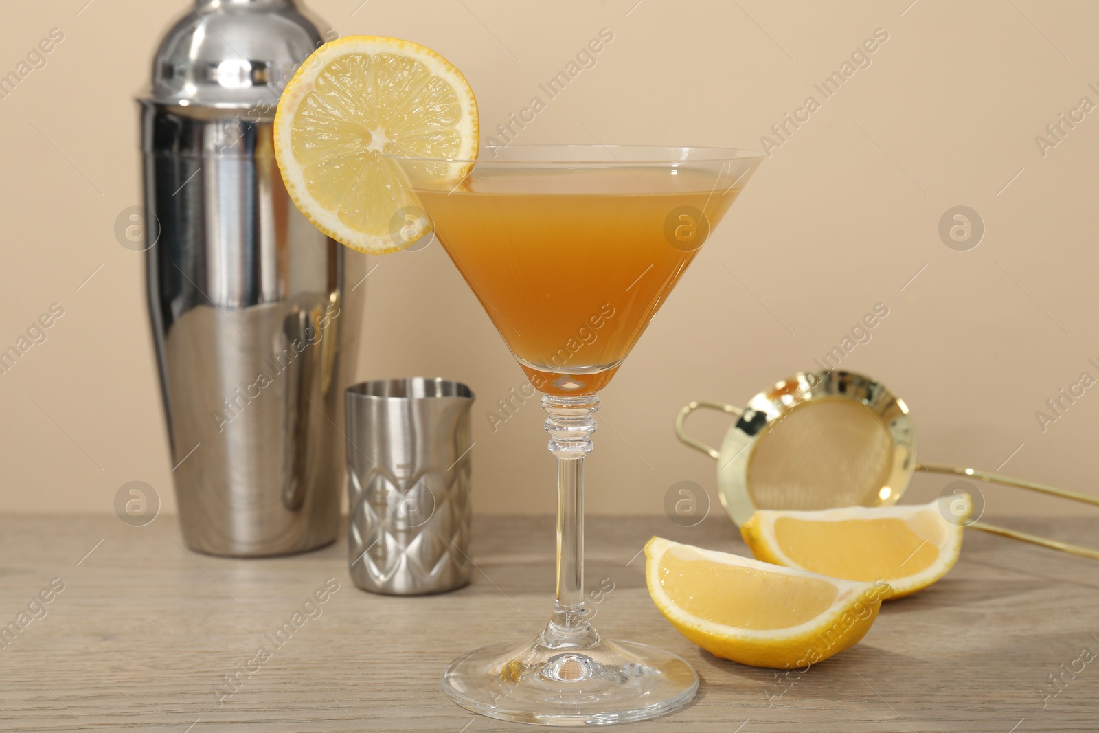 Tasty lemon cocktail in glass and bartender equipment on wooden table against beige background, closeup Photo of Tasty lemon cocktail in glass and bartender equipment on wooden table against beige background, closeup