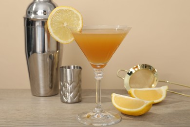 Photo of Tasty lemon cocktail in glass and bartender equipment on wooden table against beige background, closeup
