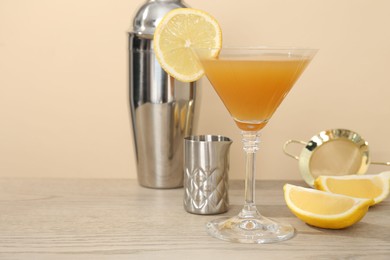 Photo of Tasty lemon cocktail in glass and bartender equipment on wooden table against beige background, closeup