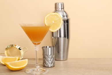 Photo of Tasty lemon cocktail in glass and bartender equipment on wooden table against beige background, closeup. Space for text