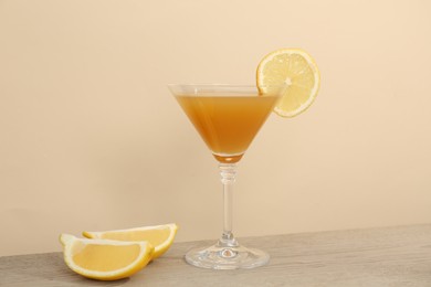 Photo of Tasty lemon cocktail in glass and fresh fruit pieces on wooden table against beige background