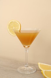 Photo of Tasty lemon cocktail in glass and fresh fruit pieces on wooden table against beige background
