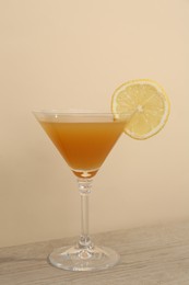 Photo of Tasty lemon cocktail in glass on wooden table near beige wall