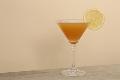Photo of Tasty lemon cocktail in glass on wooden table near beige wall, closeup. Space for text