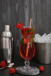 Photo of Refreshing strawberry cocktail in glass, metal shaker and ice in bucket on dark table