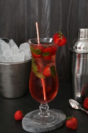 Photo of Refreshing strawberry cocktail in glass, metal shaker and ice in bucket on dark table