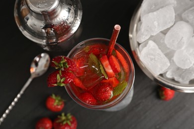 Photo of Refreshing strawberry cocktail in glass, metal shaker and ice in bucket on dark table, flat lay