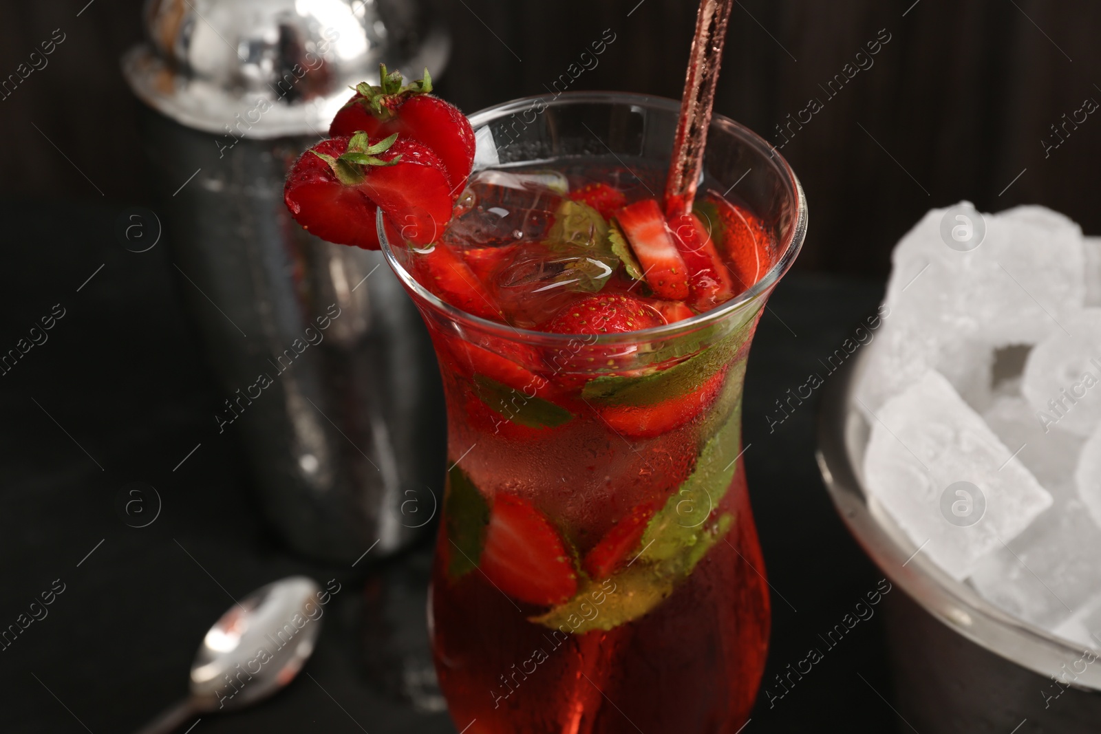 Refreshing strawberry cocktail in glass, metal shaker and ice in bucket on dark table, closeup Photo of Refreshing strawberry cocktail in glass, metal shaker and ice in bucket on dark table, closeup
