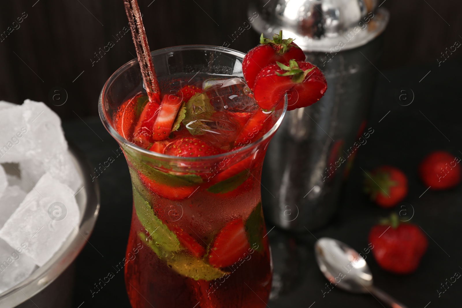 Refreshing strawberry cocktail in glass, metal shaker and ice in bucket on dark table, closeup Photo of Refreshing strawberry cocktail in glass, metal shaker and ice in bucket on dark table, closeup