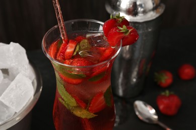 Photo of Refreshing strawberry cocktail in glass, metal shaker and ice in bucket on dark table, closeup