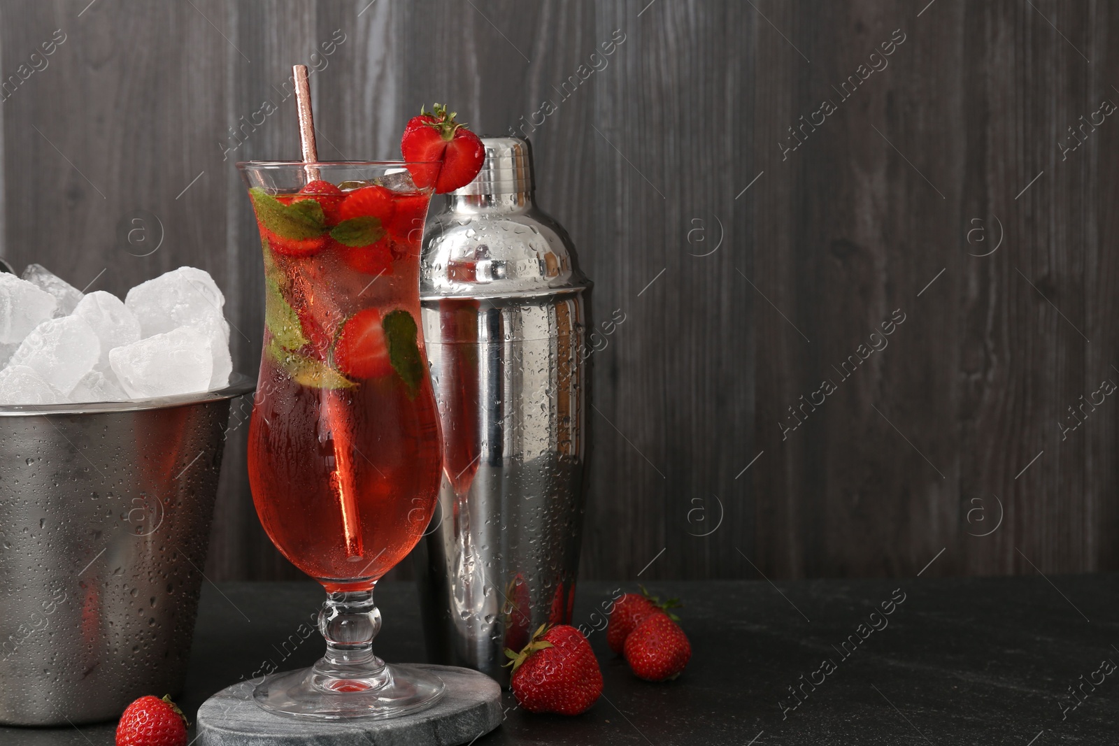 Refreshing strawberry cocktail in glass, metal shaker and ice in bucket on dark table. Space for text Photo of Refreshing strawberry cocktail in glass, metal shaker and ice in bucket on dark table. Space for text