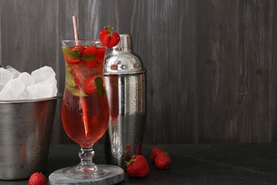 Photo of Refreshing strawberry cocktail in glass, metal shaker and ice in bucket on dark table. Space for text
