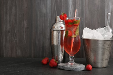 Photo of Refreshing strawberry cocktail in glass, metal shaker and ice in bucket on dark table. Space for text