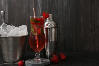 Photo of Refreshing strawberry cocktail in glass, metal shaker and ice in bucket on dark table. Space for text