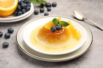 Photo of Tasty panna cotta with orange, blueberries and mint on light grey table, closeup