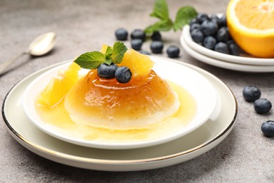 Photo of Tasty panna cotta with orange, blueberries and mint on light grey table, closeup