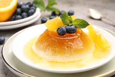 Photo of Tasty panna cotta with orange, blueberries and mint on light grey table, closeup
