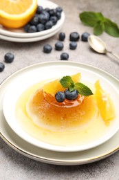 Photo of Tasty panna cotta with orange, blueberries and mint on light grey table, closeup