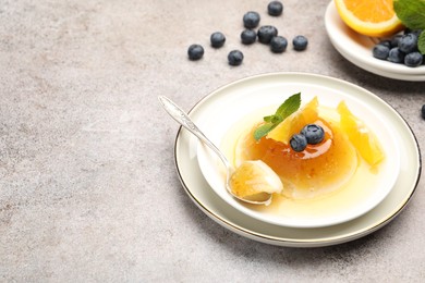 Photo of Tasty panna cotta with orange, blueberries and mint on light grey table, closeup. Space for text