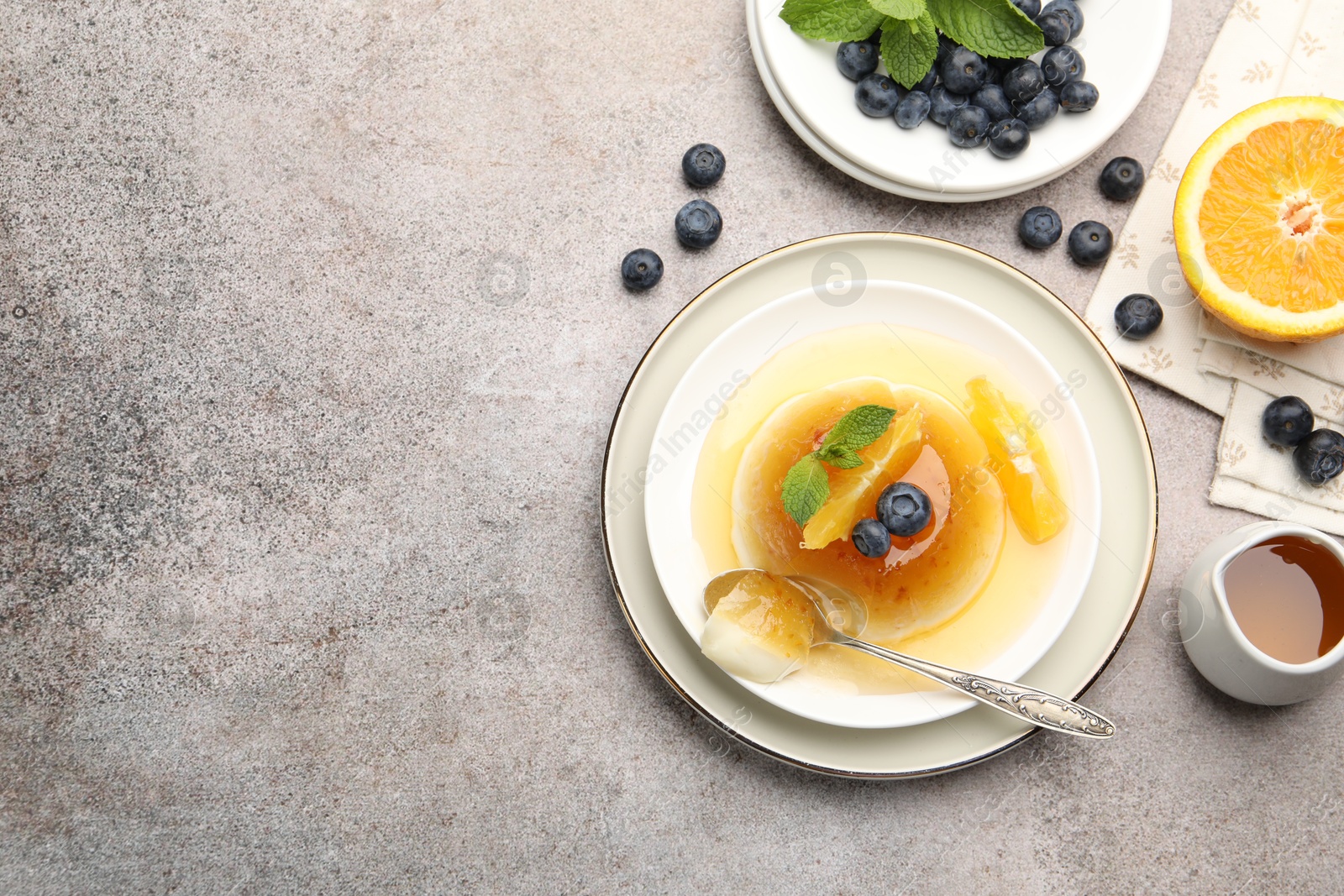 Photo of Tasty panna cotta with orange, blueberries and mint on light grey table, flat lay. Space for text