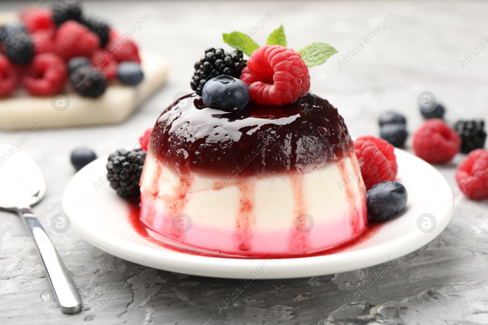 Photo of Tasty panna cotta with berries and jam on light grey table, closeup