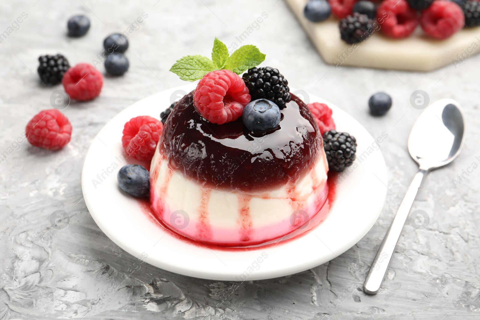 Photo of Tasty panna cotta with berries and jam on light grey table, closeup