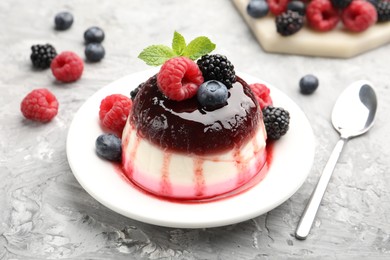 Photo of Tasty panna cotta with berries and jam on light grey table, closeup