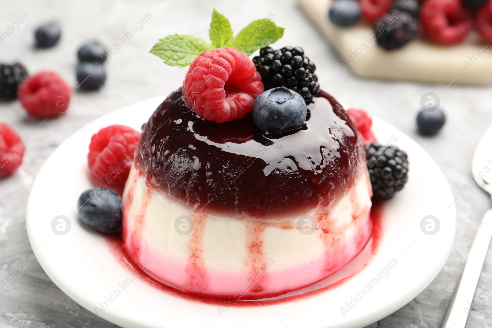 Tasty panna cotta with berries and jam on light grey table, closeup Photo of Tasty panna cotta with berries and jam on light grey table, closeup