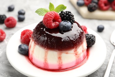 Photo of Tasty panna cotta with berries and jam on light grey table, closeup