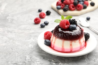 Photo of Tasty panna cotta with berries and jam on light grey table, closeup. Space for text