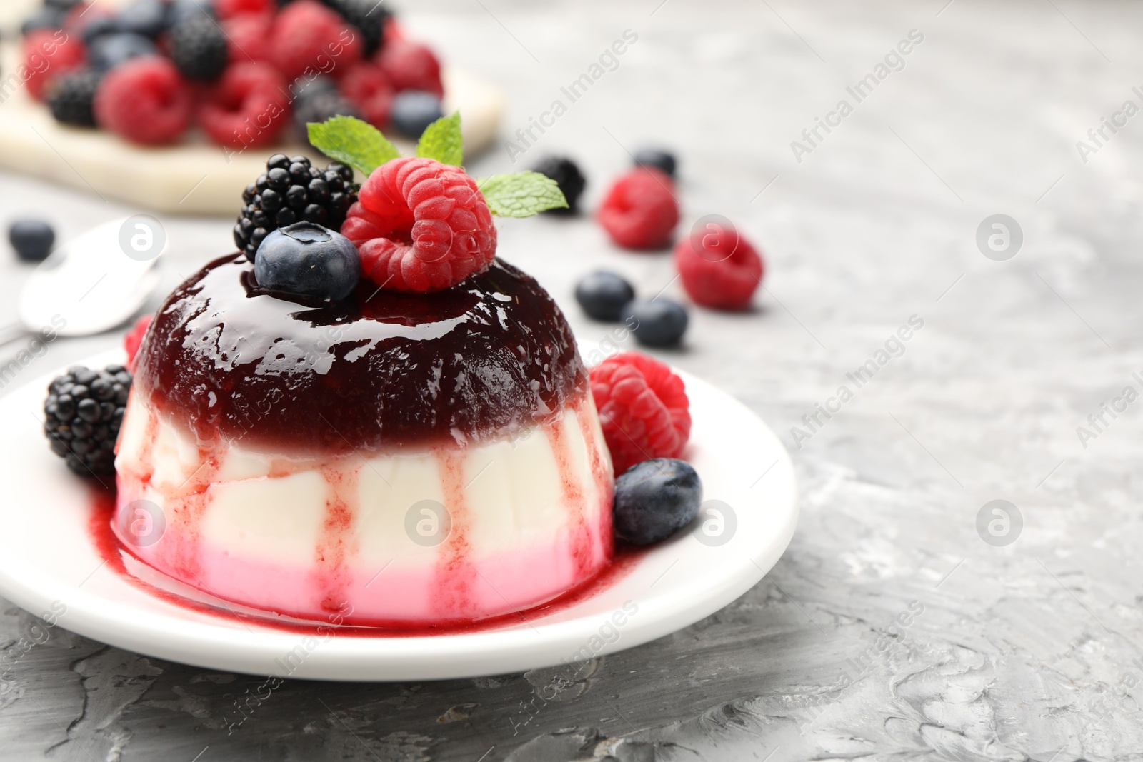 Photo of Tasty panna cotta with berries and jam on light grey table, closeup. Space for text