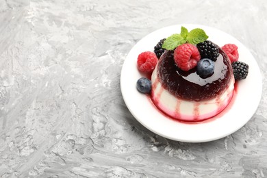 Photo of Tasty panna cotta with berries and jam on light grey table, space for text