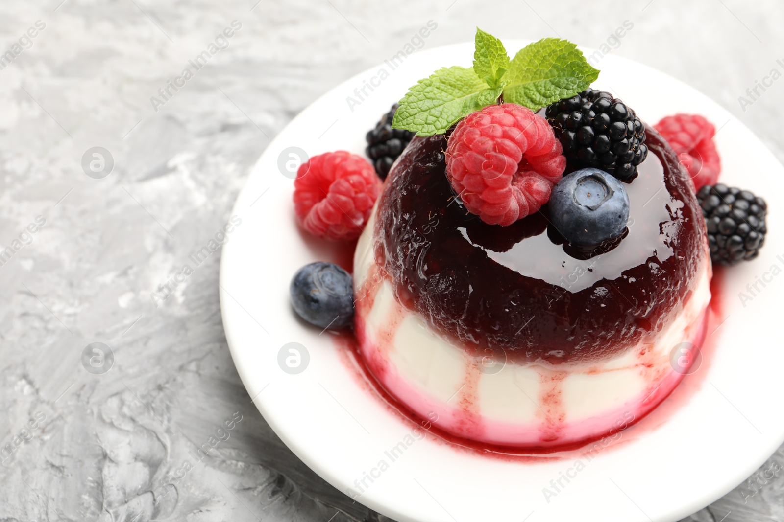 Photo of Tasty panna cotta with berries and jam on light grey table, closeup