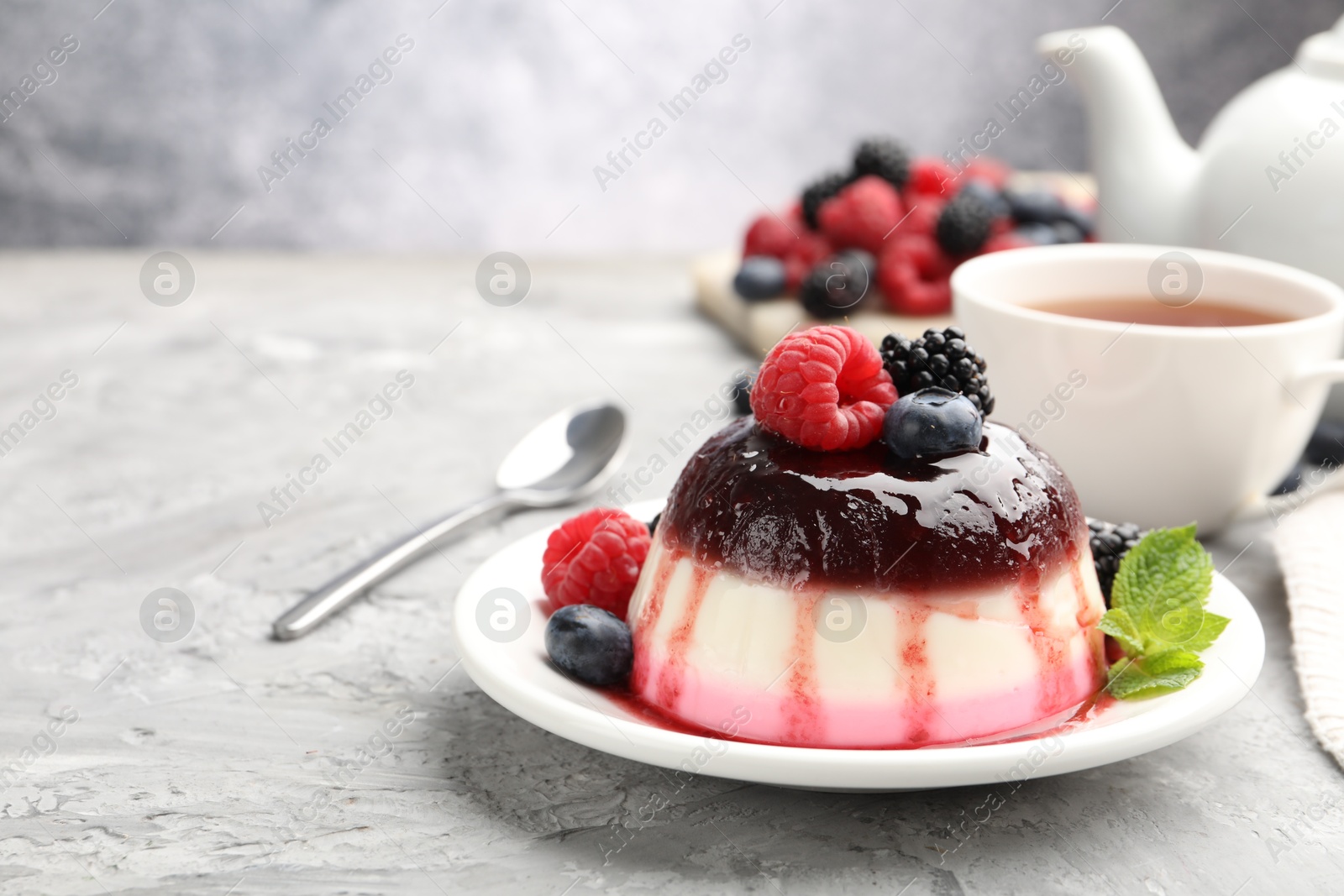 Photo of Tasty panna cotta with berries and jam on light grey table, closeup. Space for text