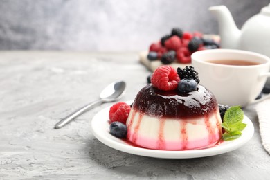 Photo of Tasty panna cotta with berries and jam on light grey table, closeup. Space for text